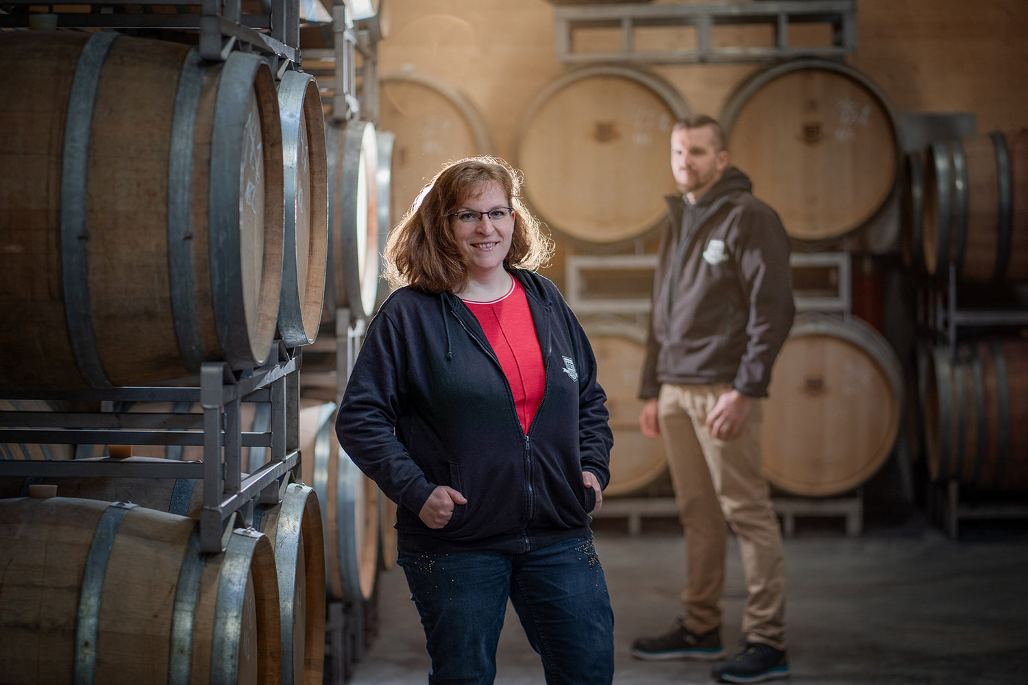 Katja Nett mit Ehemann Christian Nett im Hintergrund vor Holzfässen in der Kellerei