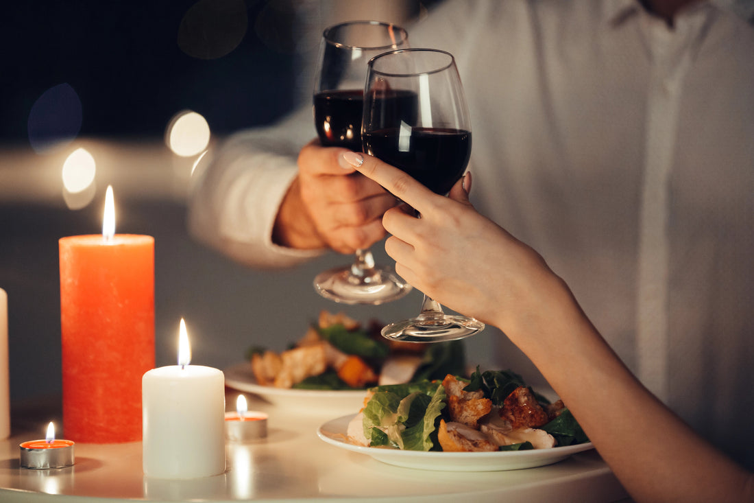 Paar stößt bei einem romantischen Abendessen mit alkoholfreiem Rotwein an, umgeben von Kerzenlicht und entspannter Atmosphäre.